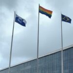 Fachada da Câmara Legislativa do DF em dia nublado com bandeira arco-íris desbotada, representando Programa Reconhecer e falhas na proteção LGBTQIAPN+.