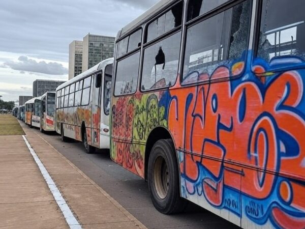Ônibus vandalizados em rua de Brasília, com danos como vidros quebrados e pichações, em investigação da PCDF.