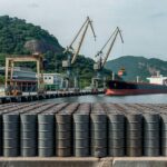 Barris de petróleo em porto brasileiro, representando tensões no mercado global de óleo.
