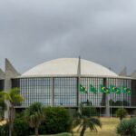 Edifício da Câmara Legislativa do DF em Brasília sob céu nublado, com elementos de burocracia e lentidão legislativa.