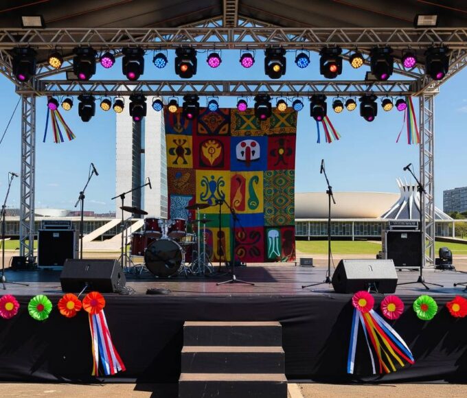 Palco preparado para festa de axé no DF, com equipamentos de som e decorações coloridas, arquitetura de Brasília ao fundo.