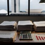 Mesa com documentos fiscais e gráficos de declínio econômico em Brasília, criticando alta carga tributária.
