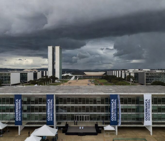 Edifício da CLDF em Brasília com decorações de evento de governança e nuvens escuras ao fundo, representando distração para crises no DF.