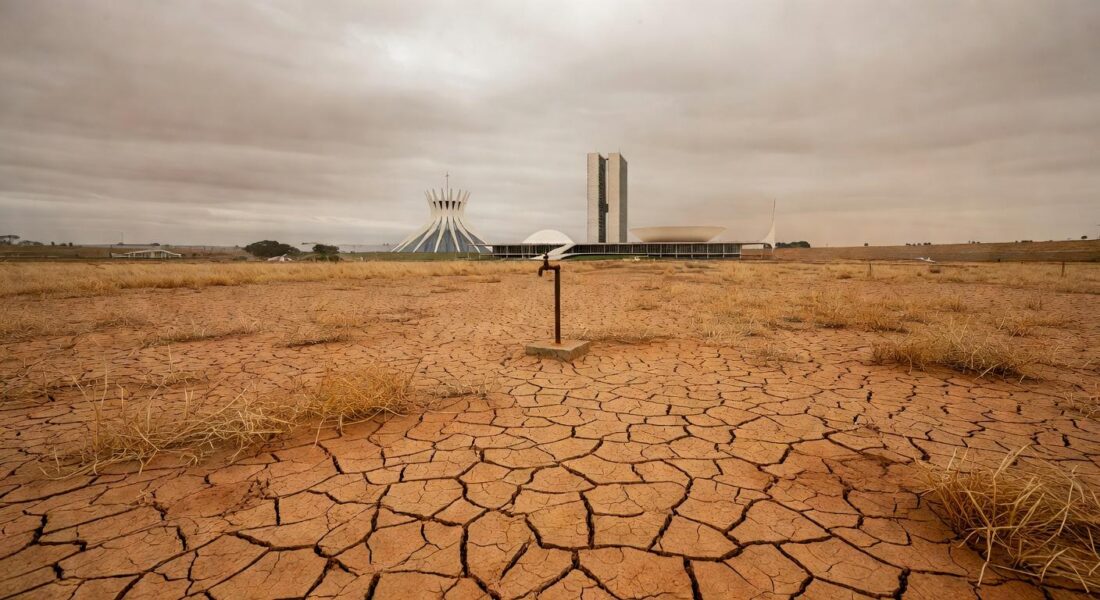 Praça em Brasília com local vazio para ponto de hidratação, arquitetura modernista ao fundo, destacando atraso e riscos à saúde.