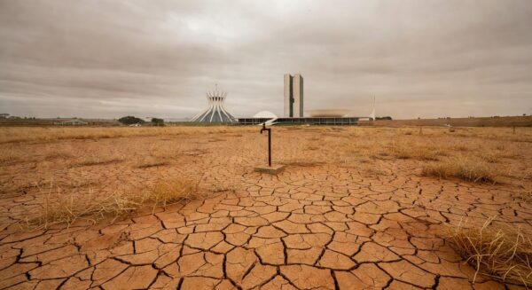 Praça em Brasília com local vazio para ponto de hidratação, arquitetura modernista ao fundo, destacando atraso e riscos à saúde.