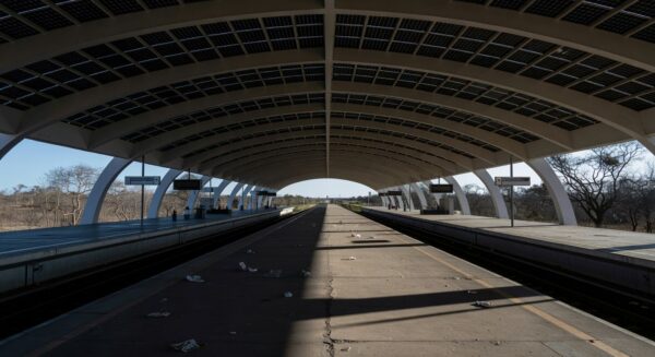 Estação de metrô em Brasília com trilhos vazios e documentos burocráticos, representando atrasos em contratações no Metrô-DF.